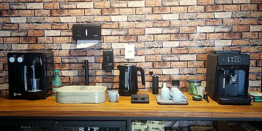 Bancada de café com máquinas, xícaras e parede de tijolos ao fundo